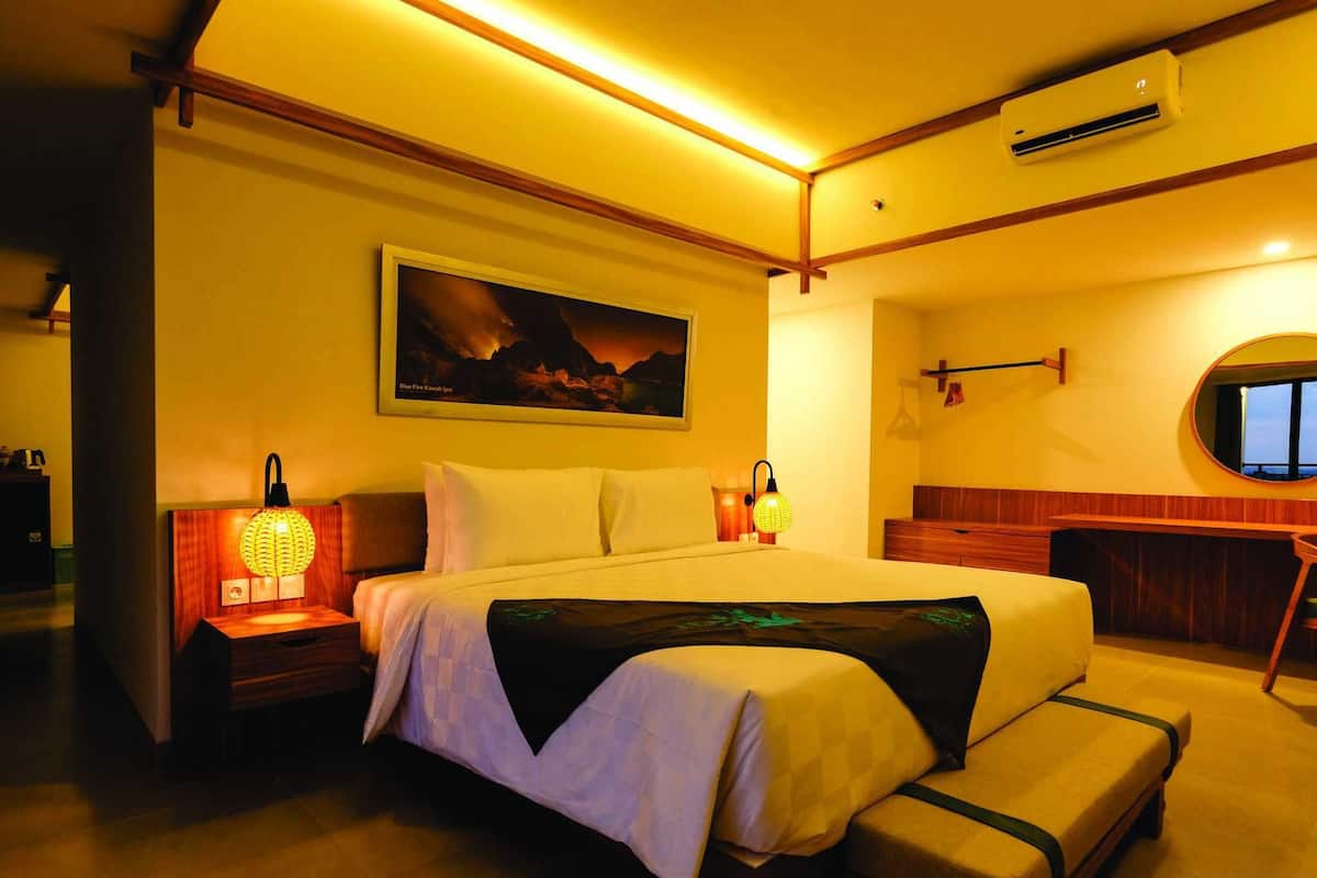 Hotelkamer met groot bed, bedlampen, schilderij aan de muur, airconditioning en uitzicht door een raam.