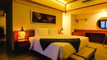A hotel room with a large bed, bedside lamps, a painting on the wall, an air conditioning unit, and a view through a window.