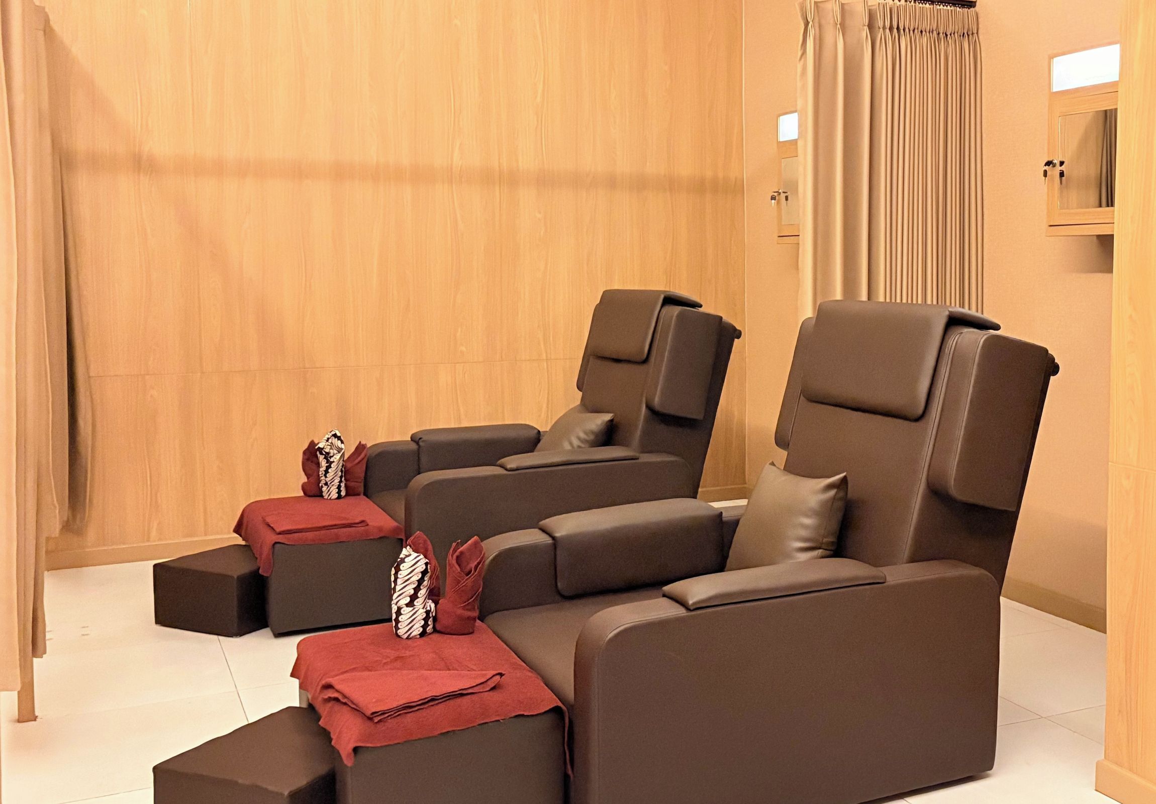 A room with three reclining massage chairs, a wooden wall, and a window with curtains.