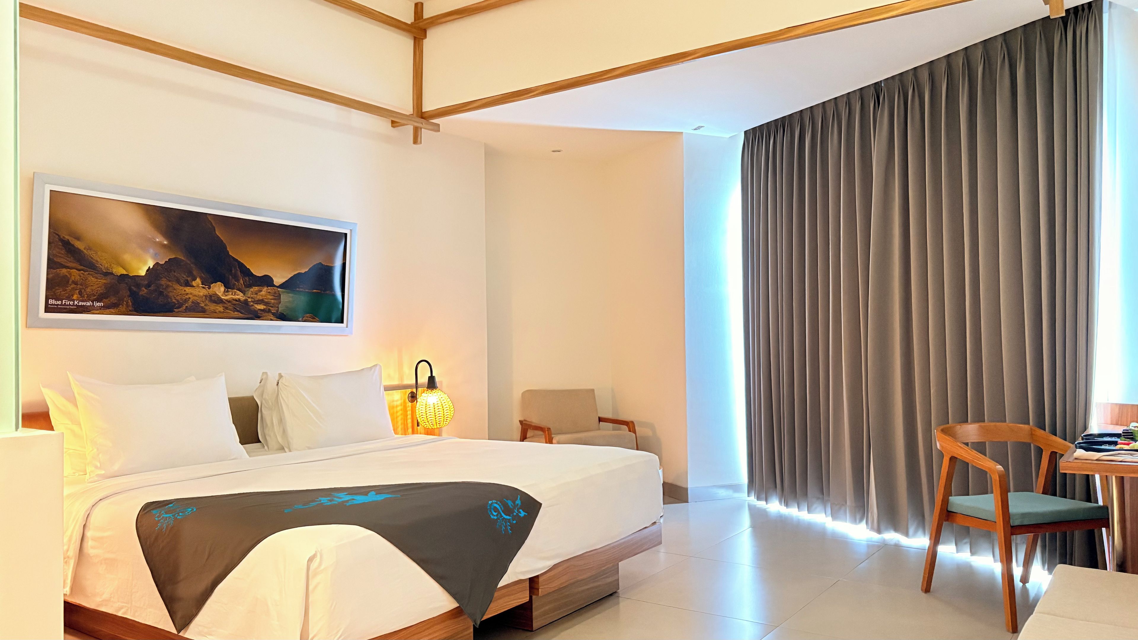 A hotel room with a bed, a chair, a desk, and a large window with curtains.
