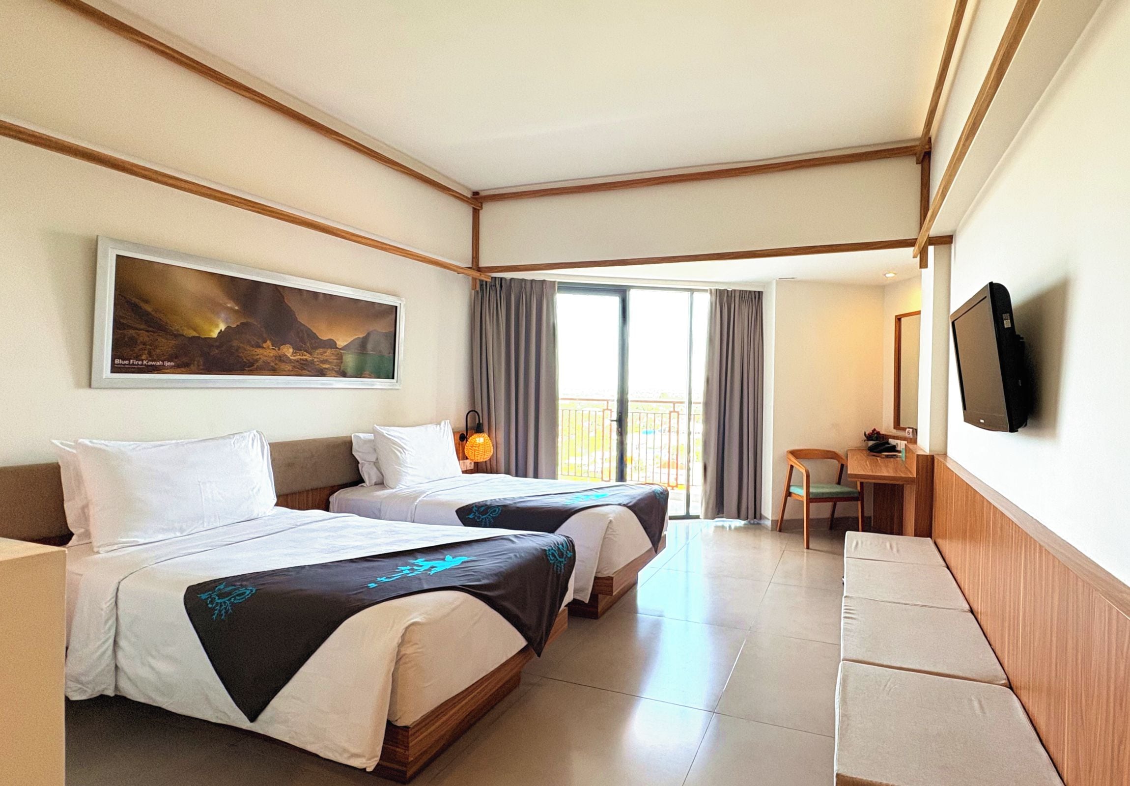 Une chambre d’hôtel avec deux lits, une grande fenêtre, un tableau, un bureau avec une chaise et un téléviseur.