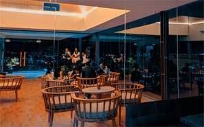 Un espace de détente moderne avec des tables et des chaises rondes en bois, et de grandes fenêtres offrant une vue sur la ville la nuit.