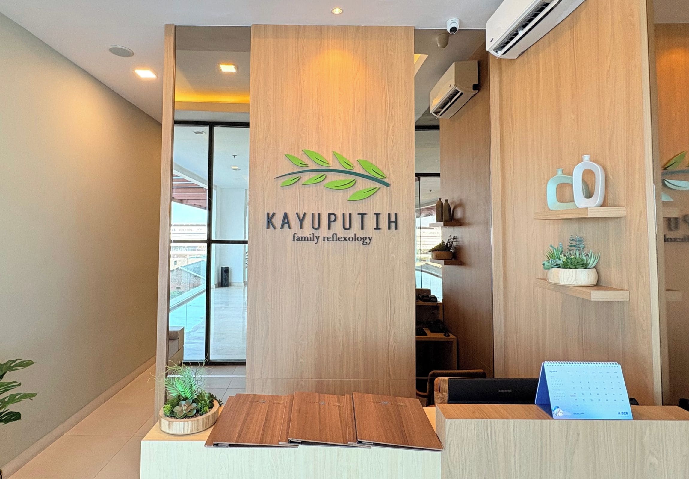 A reception desk with a logo for 'Kayuputhih family reflexology' and a calendar on the right.