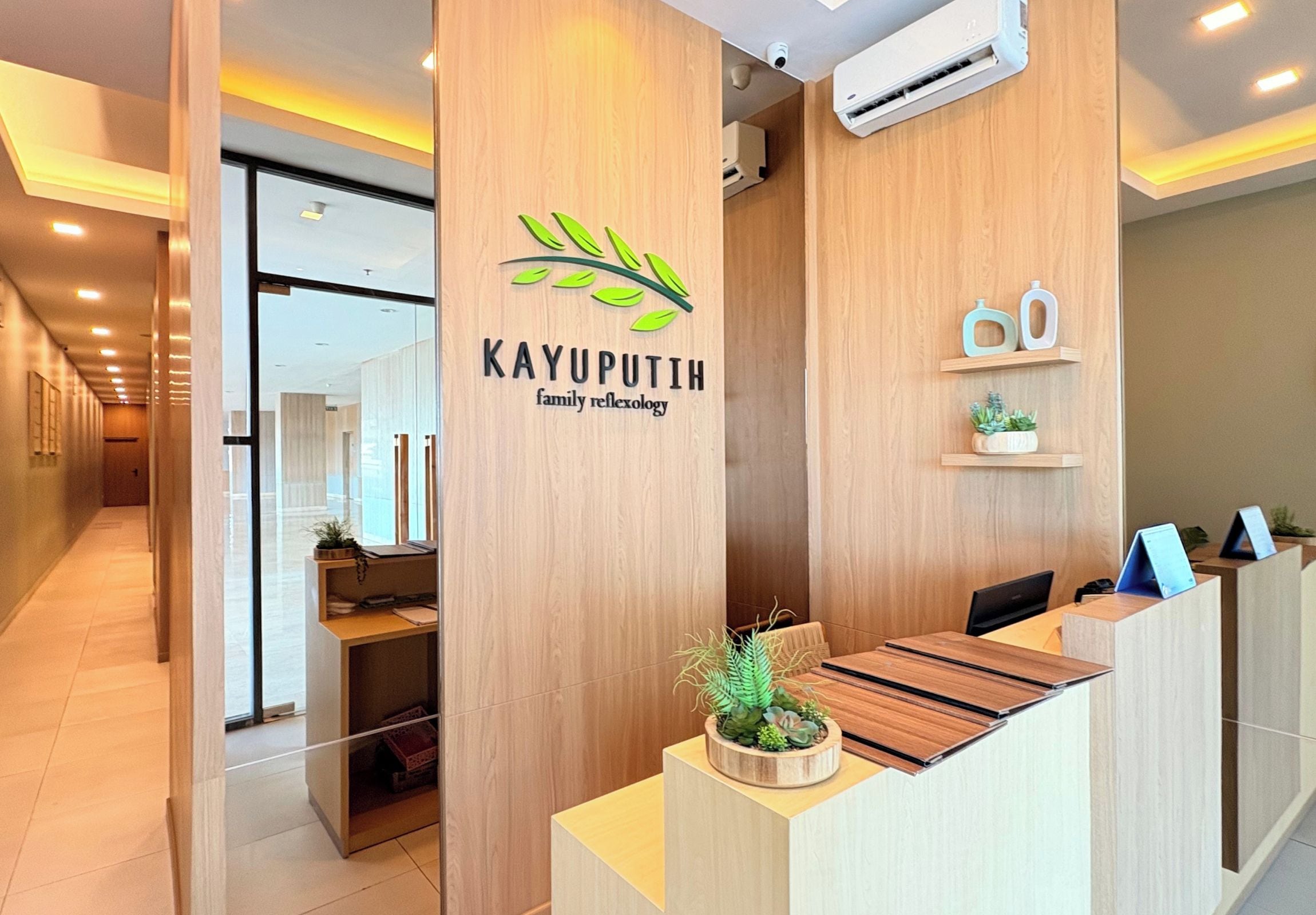 A reception desk with a logo for 'KAYUPUTIH family reflexology' and a plant on the counter.