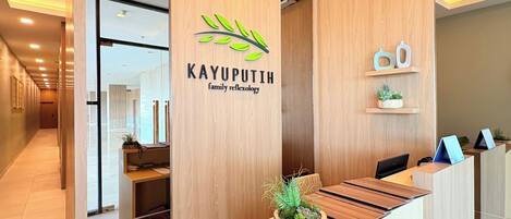 A reception desk with a logo for 'KAYUPUTIH family reflexology' and a plant on the counter.