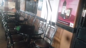 A restaurant interior with multiple tables and chairs, a poster on the wall, and a window with bars. - Magi Guest House (Thika)
