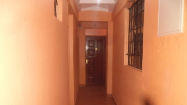 A corridor with a door at the end, a window with bars on the right, and a light fixture on the ceiling. - Magi Guest House (Thika)