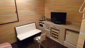 Ein kompaktes Hotelzimmer mit einer Schlafcouch, einem Fernseher, einer Mikrowelle, einem kleinen Kühlschrank und einem Tisch mit einer Flasche und Taschentüchern.