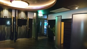 Ein moderner Flur mit Glastür zu einem Raum, einer Pflanze und einer Wandleuchte.