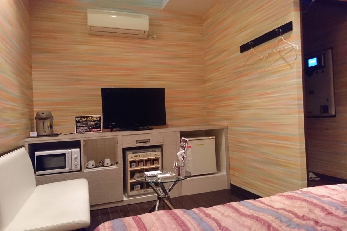 Ein Hotelzimmer mit Bett, Fernseher, Mikrowelle, Kühlschrank und einer kleinen Küchenzeile.