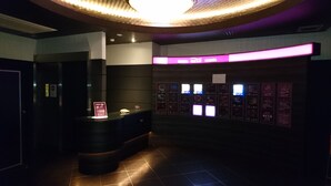 Ein Hotel-Empfangsbereich mit Theke, einem Schild, das kostenloses WLAN anbietet, und mehreren beleuchteten Tafeln, vermutlich mit Zimmerinformationen.