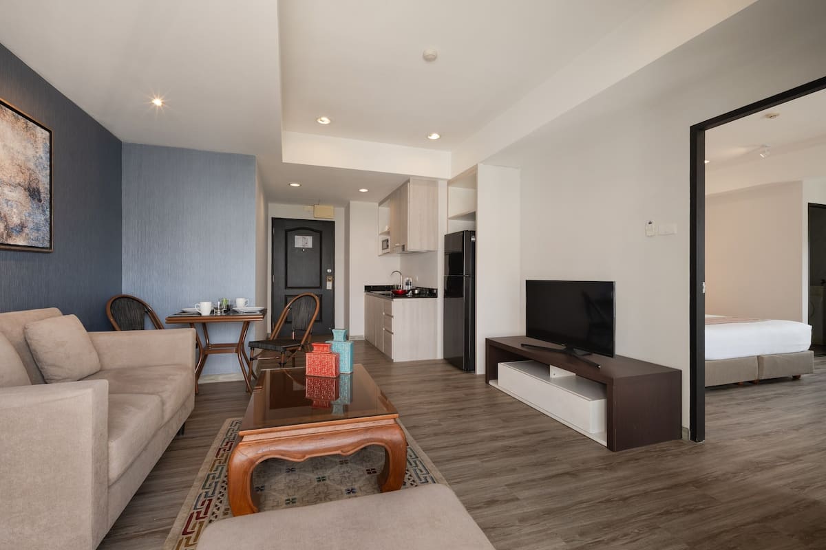 A modern hotel room with a living area, kitchenette, and a separate bedroom.