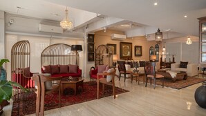 A spacious living room with a red sofa, wooden chairs, and a coffee table. There are decorative items and a chandelier. - Aspira Residence Ruamrudee (Bangkok)