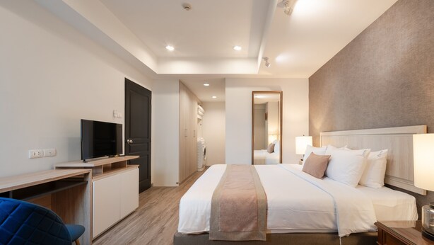 A modern hotel room with a bed, bedside table, lamp, TV, desk, and chair. - Aspira Residence Ruamrudee (Bangkok)