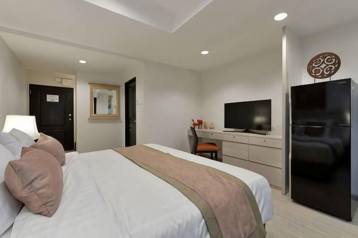 A modern hotel room with a bed, a desk, a television, and a refrigerator.