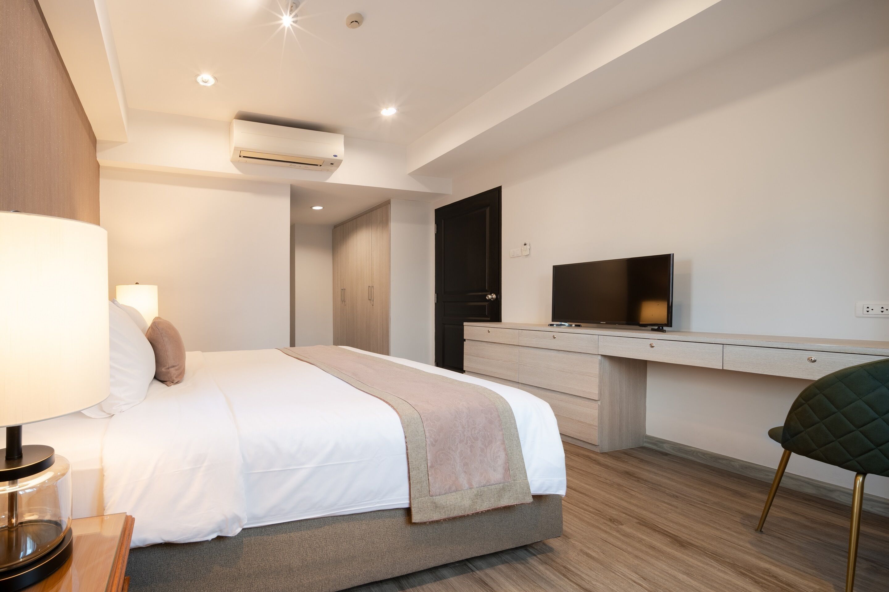 Moderni hotellihuone, jossa on sänky, yöpöytä, lamppu, televisio ja työpöytä tuolilla.