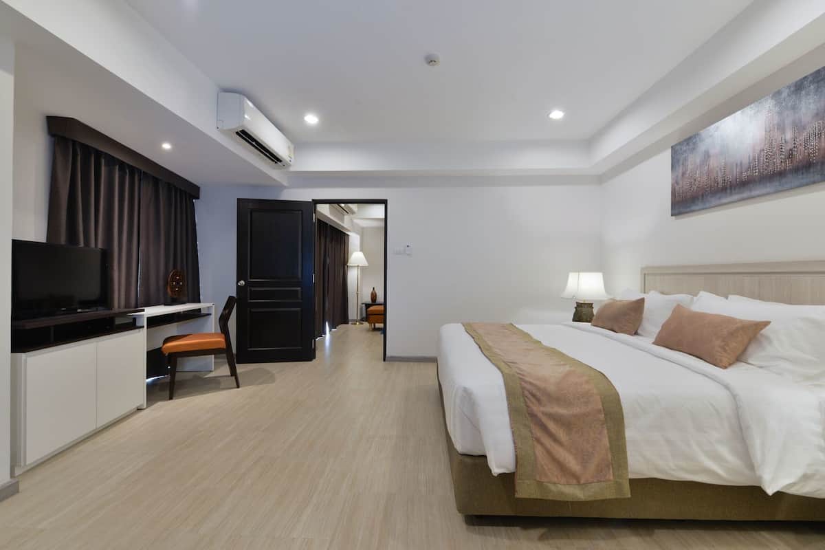 A hotel room with a bed, TV, desk, chair, and an air conditioning unit.
