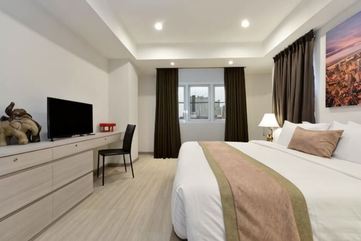 A hotel room with a bed, a desk, a chair, a television, and a window with curtains.