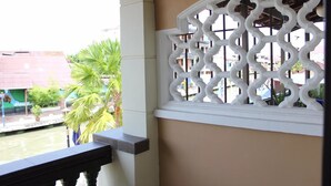 A balcony with a white decorative window and a view of a canal with palm trees.