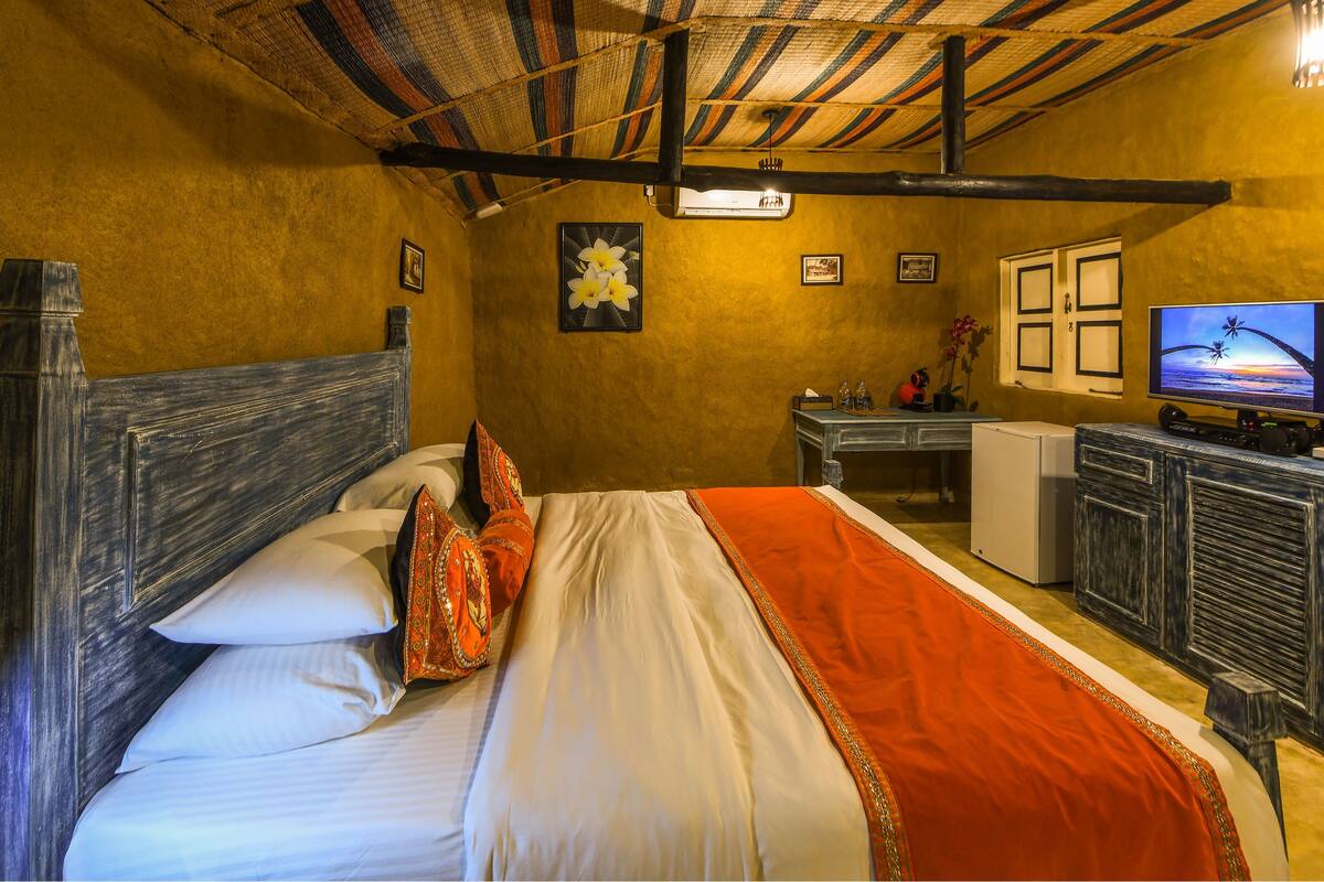 Quarto com cama, escrivaninha, televisão e ventoinha no teto.