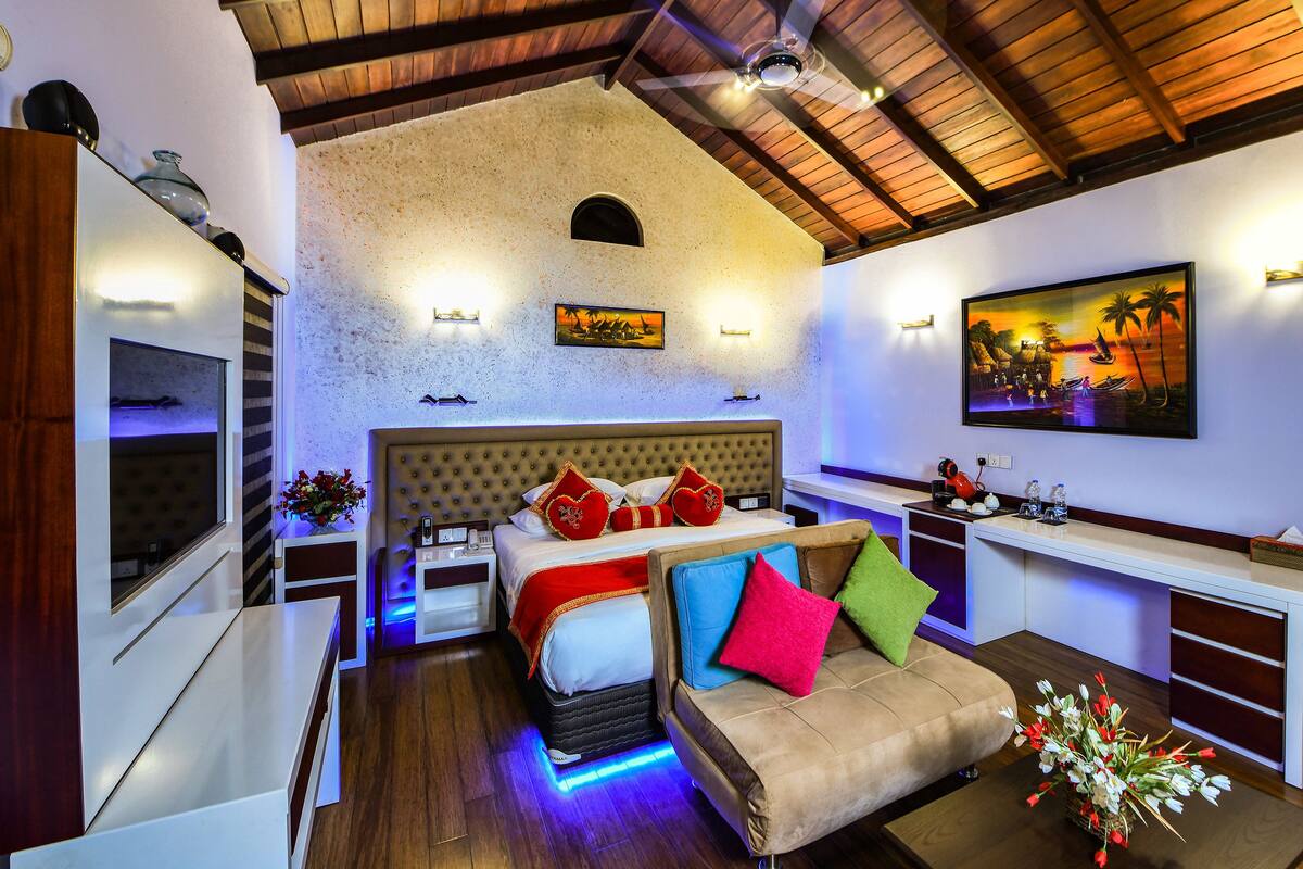 Quarto de hotel moderno com uma cama grande, um sofá, uma pequena mesa com um vaso de flores e um quadro na parede.