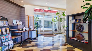 Un área de recepción con mostrador de check-in, una exhibición de revistas, una planta en maceta y suelo de baldosas.