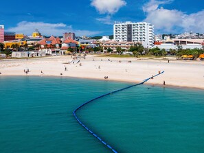 A coastal cityscape with a sandy beach, a blue water feature, and various buildings including a prominent white hotel.
