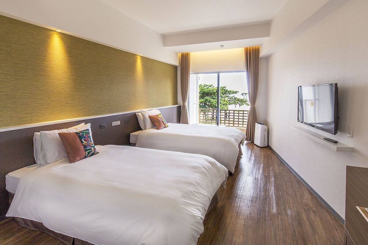 A hotel room with two beds, a TV, a window with curtains, and a ceiling light.