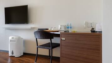 Habitación de hotel con escritorio, silla, televisión de pantalla plana, cafetera, botellas de agua y un cesto de basura.