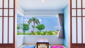 Una habitación con esteras de tatami, una mesa de madera y vista a una playa con palmeras.