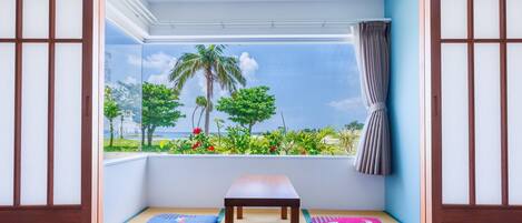 Una habitación con esteras de tatami, una mesa de madera y vista a una playa con palmeras.
