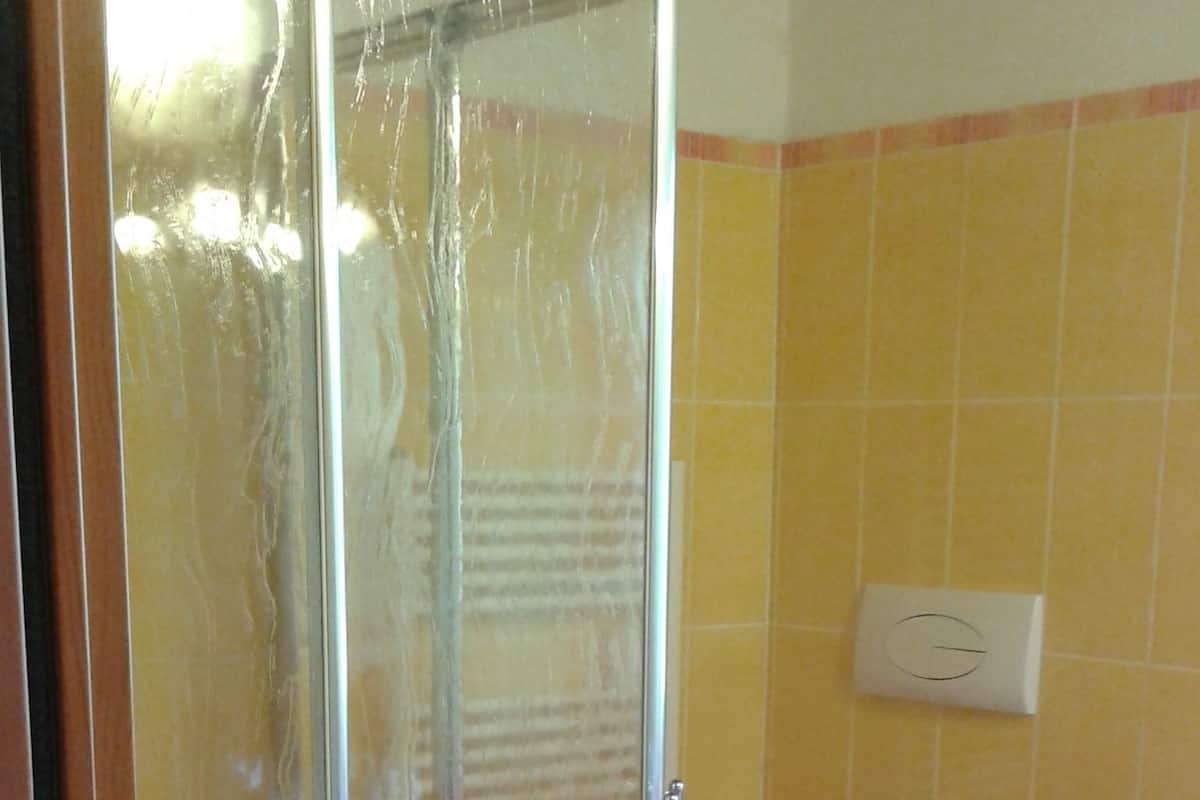 Un baño con cabina de ducha de vidrio, inodoro y toallero en la pared.