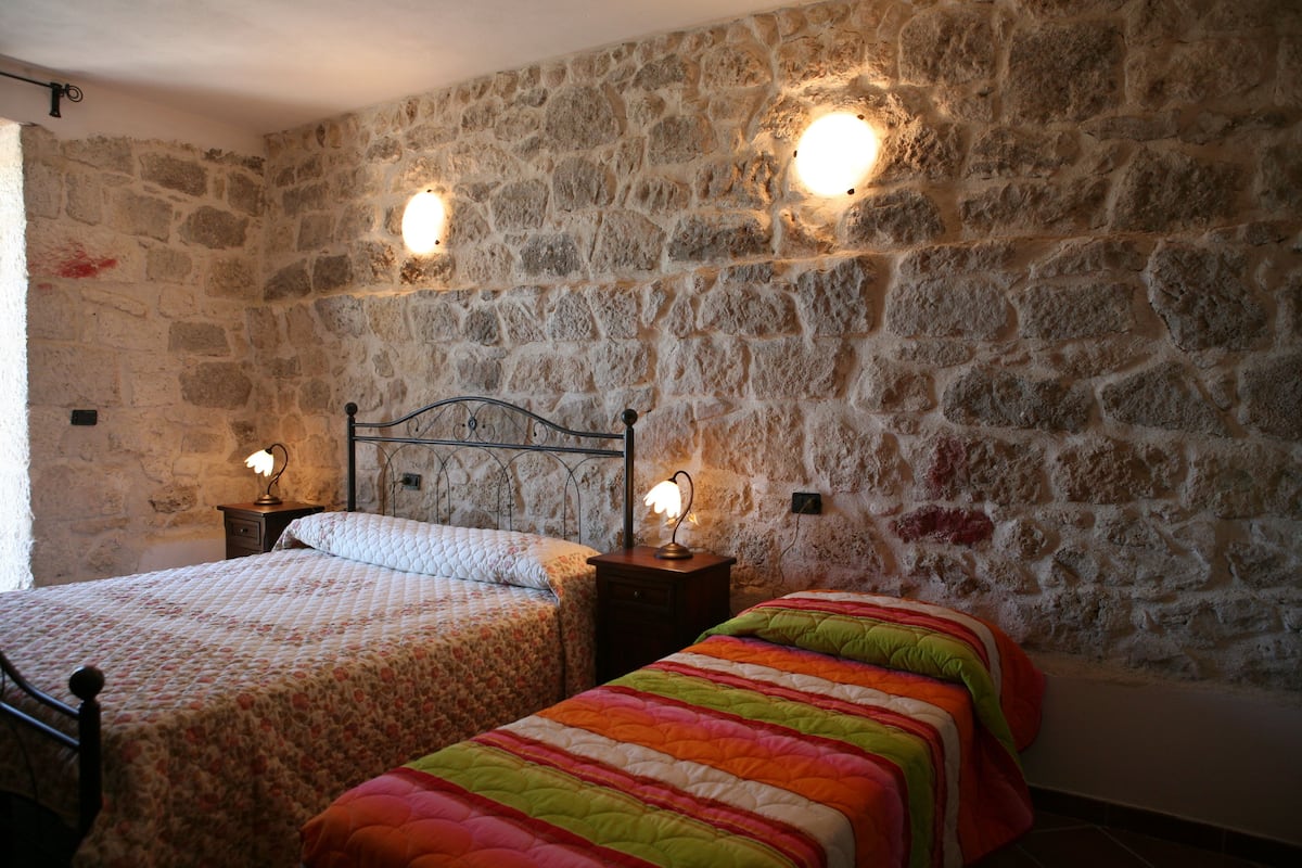 Una habitación con pared de piedra, dos camas con colchas diferentes y dos lámparas de pared.