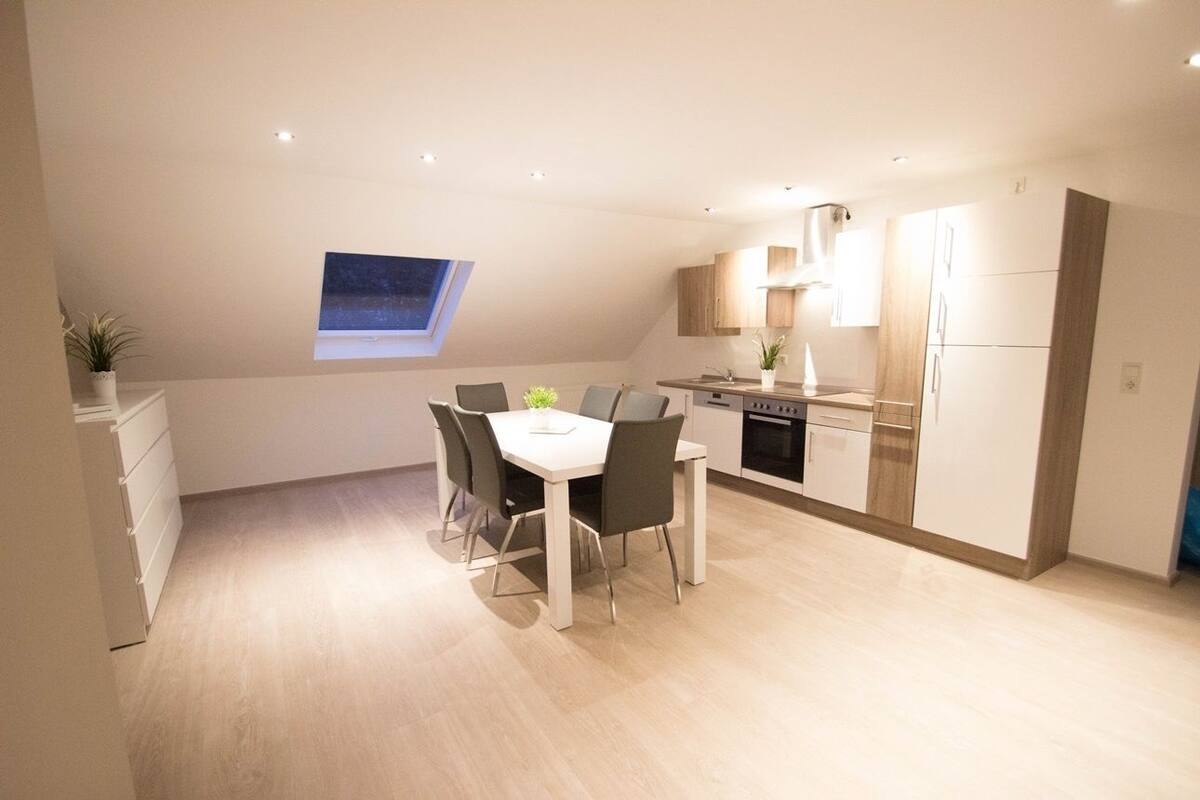 A modern kitchen with a dining area, featuring a skylight, wooden cabinets, and a white countertop.