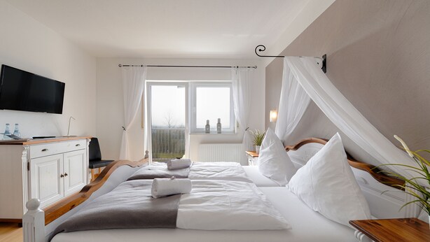 A bedroom with a bed, a TV, a window with curtains, and a view of the outdoors. - Hotel Restaurant Litermont (Nalbach)