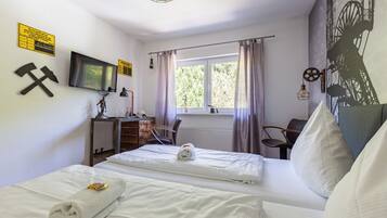 Una habitación de hotel con cama, escritorio, silla, televisión y ventana con cortinas.