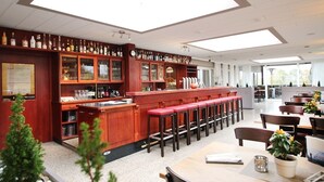 A bar area with wooden cabinets, red bar stools, and a long counter. - Hotel Restaurant Litermont (Nalbach)