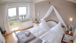 A bedroom with a double bed, a canopy bed, a window with curtains, a bedside table with a plant, and a view of the outdoors. - Hotel Restaurant Litermont (Nalbach)