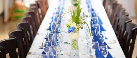Una larga mesa de comedor con manteles azules, servilletas blancas y cristalería transparente.