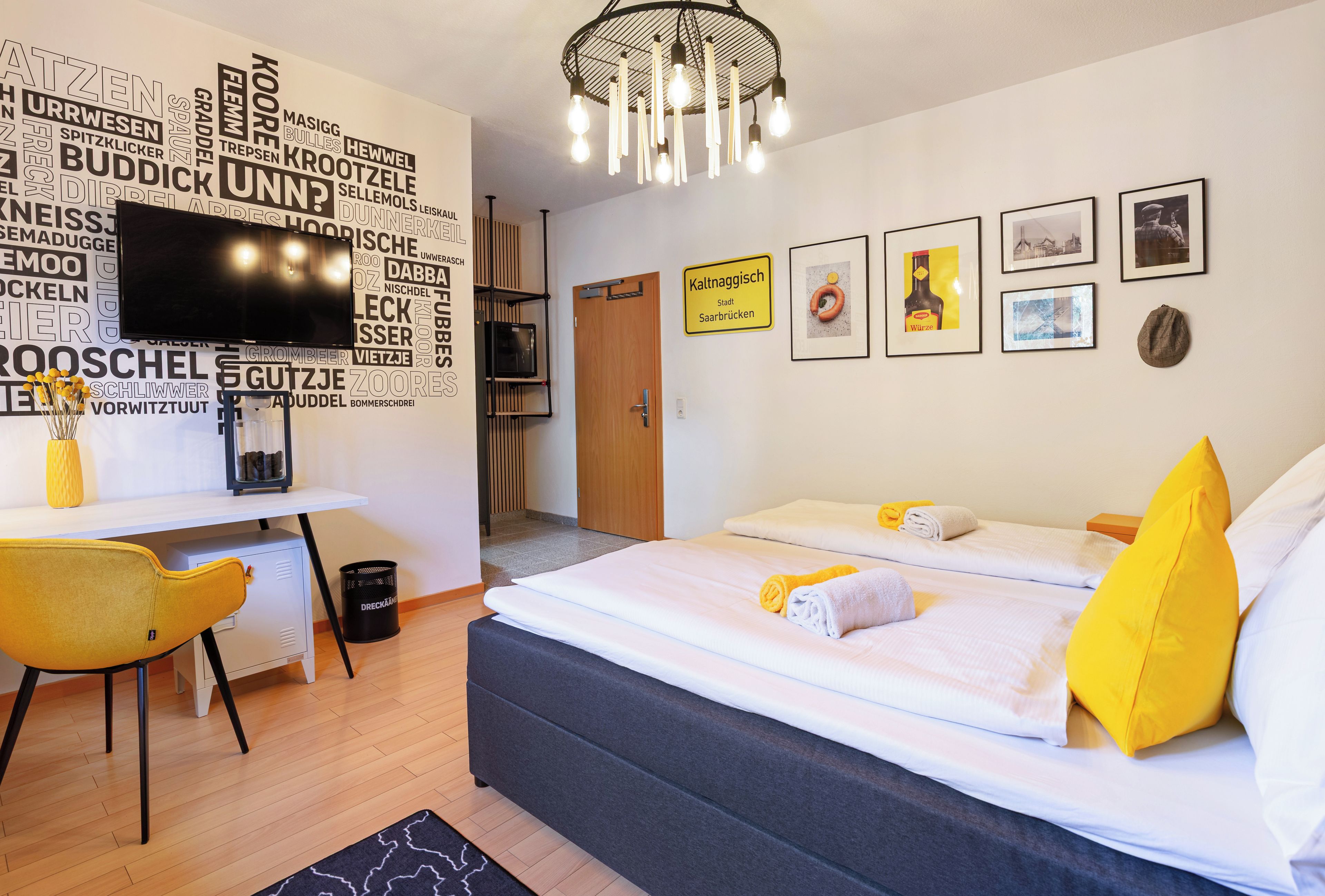 Ein modernes Hotelzimmer mit einem Bett, einem Schreibtisch, einem Fernseher und einer Wand mit verschiedenen Aufschriften.
