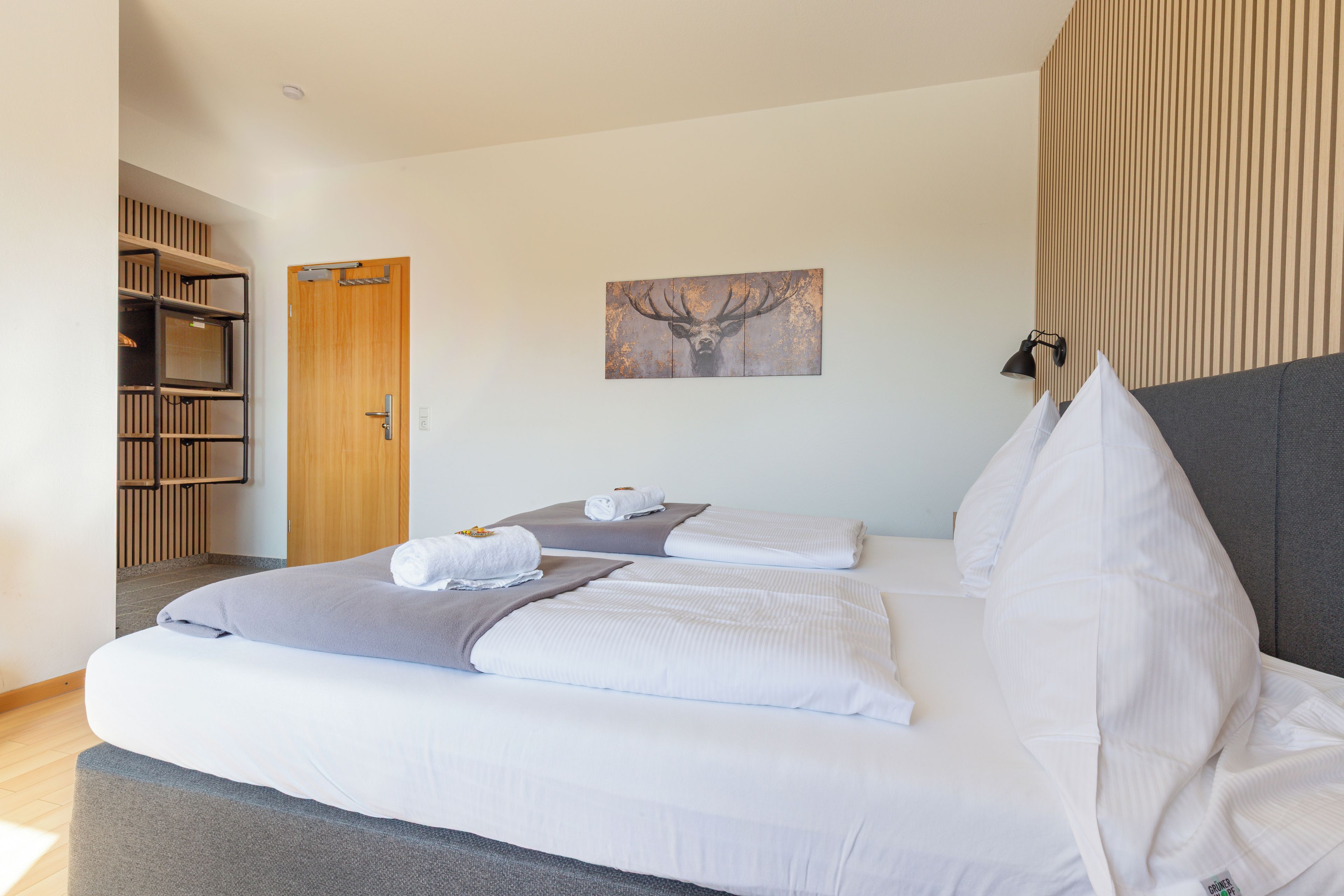 Habitación de hotel con cama, puerta de madera, cuadro colgado en la pared y lámpara de noche.