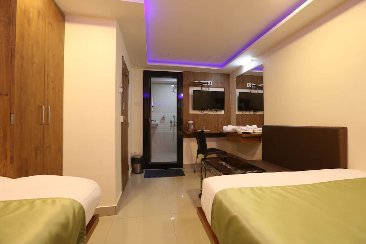 Quarto de hotel com duas camas, uma escrivaninha, uma cadeira, televisão e banheiro visível pela porta.