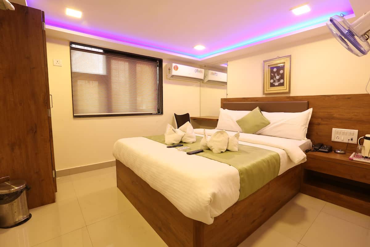 Quarto de hotel com cama, mesa de cabeceira e janela com persianas.