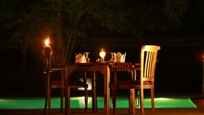 A dining table with chairs and candles, set against a dark background with a pool. - Pinthaliya Resort & Spa (Avudangawa)