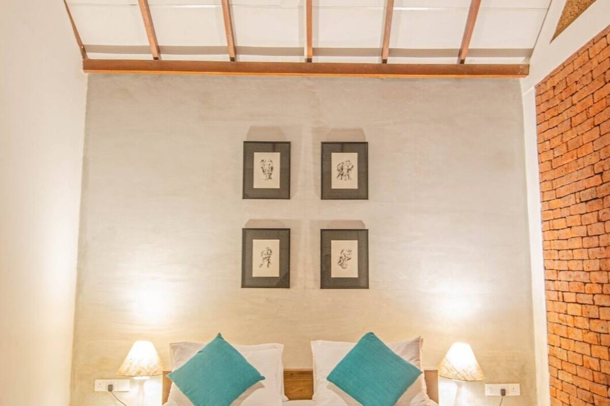 A bedroom with a wooden headboard, a bed with white bedding and teal pillows, a ceiling fan, and four framed artworks on the wall.