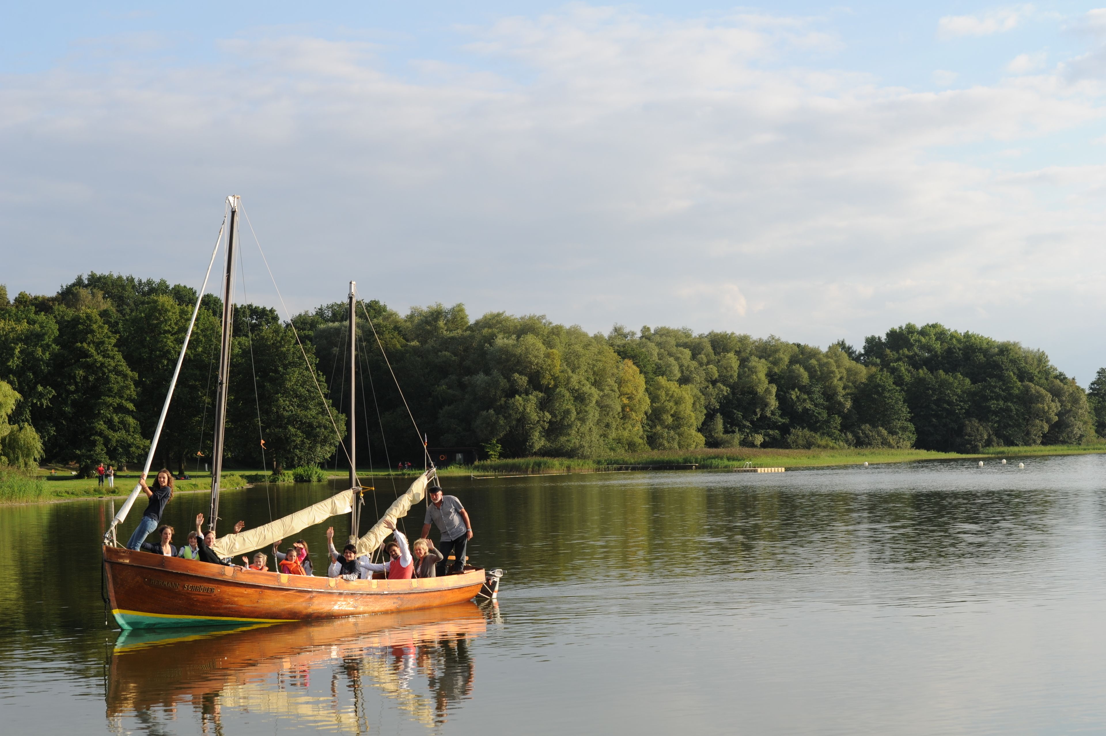 Un bote con pasajeros en un lago tranquilo, rodeado de árboles.