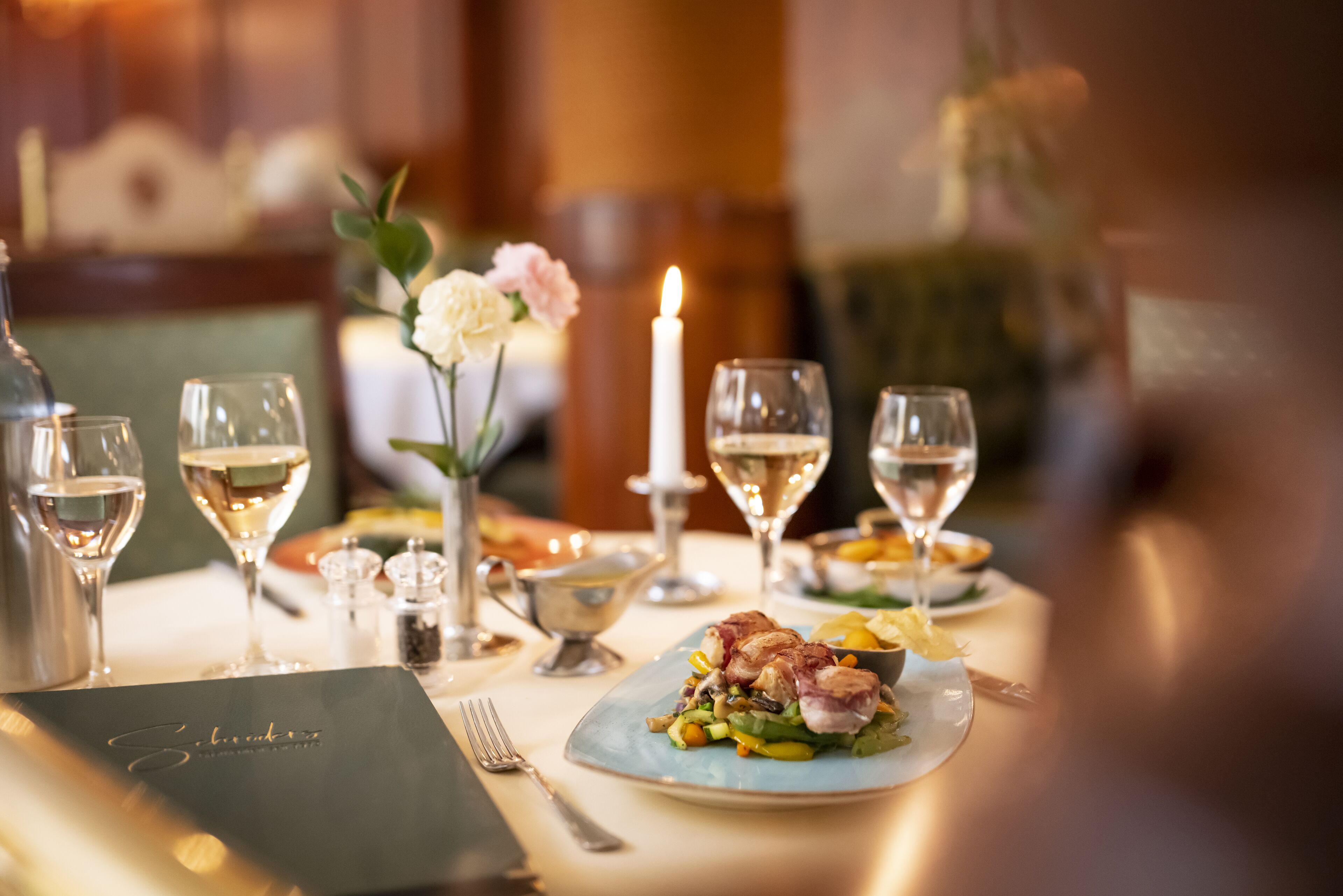 Une table à manger dressée avec des verres à vin, une bougie et un menu.