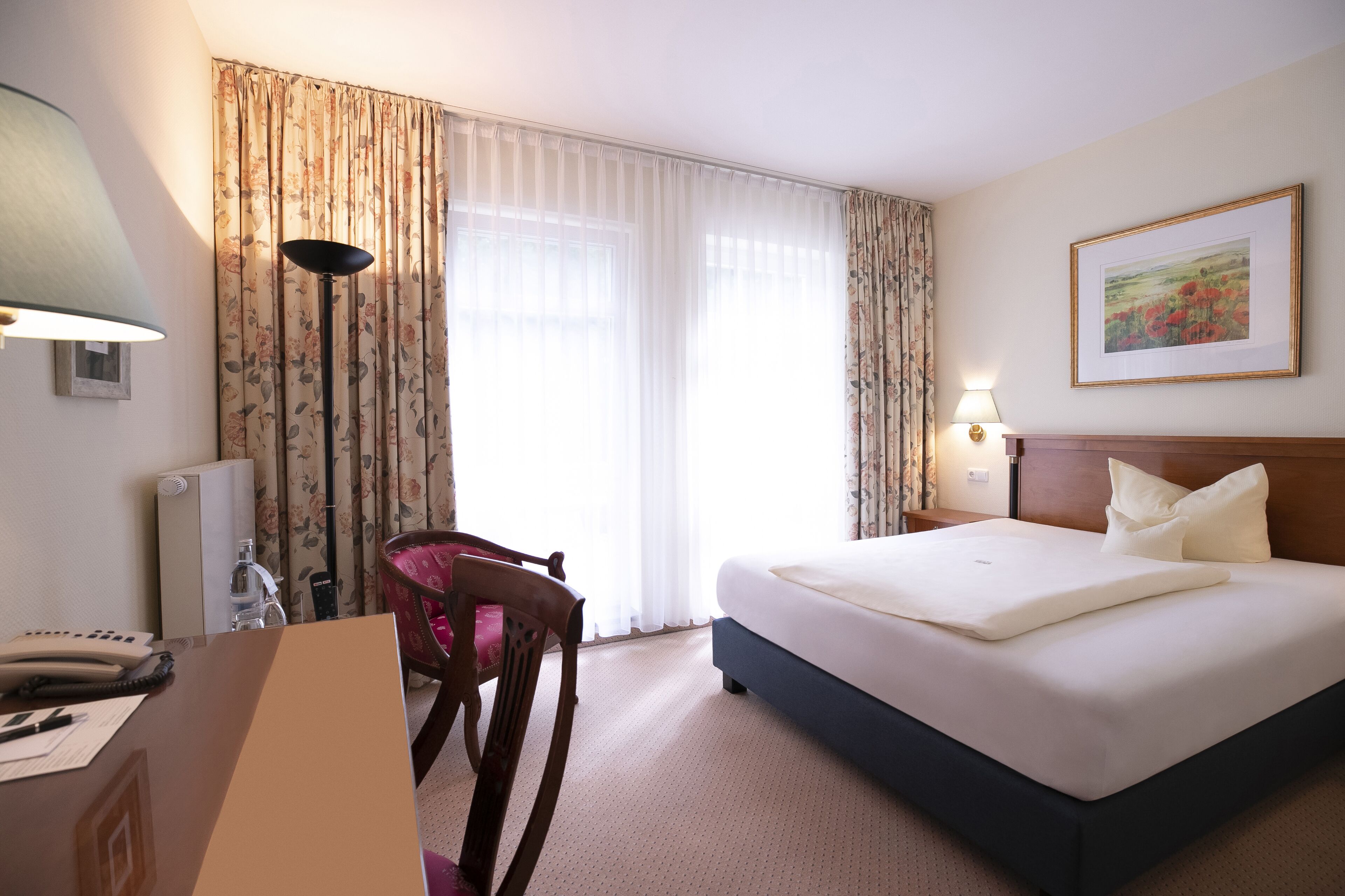 Una habitación de hotel con cama, escritorio, teléfono, silla y lámpara.