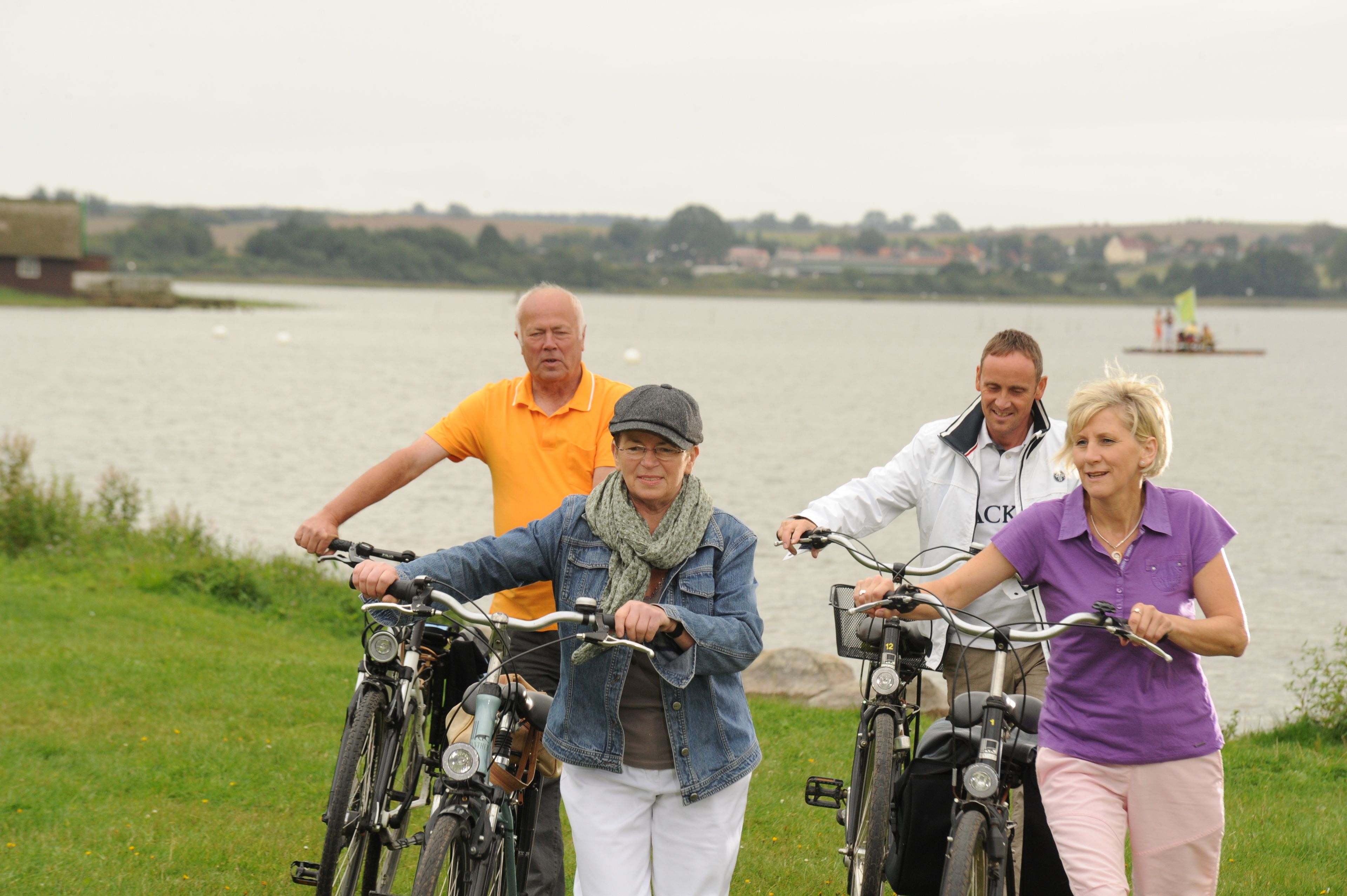 Quatre personnes à vélo près d’un lac, avec un bateau en arrière-plan.