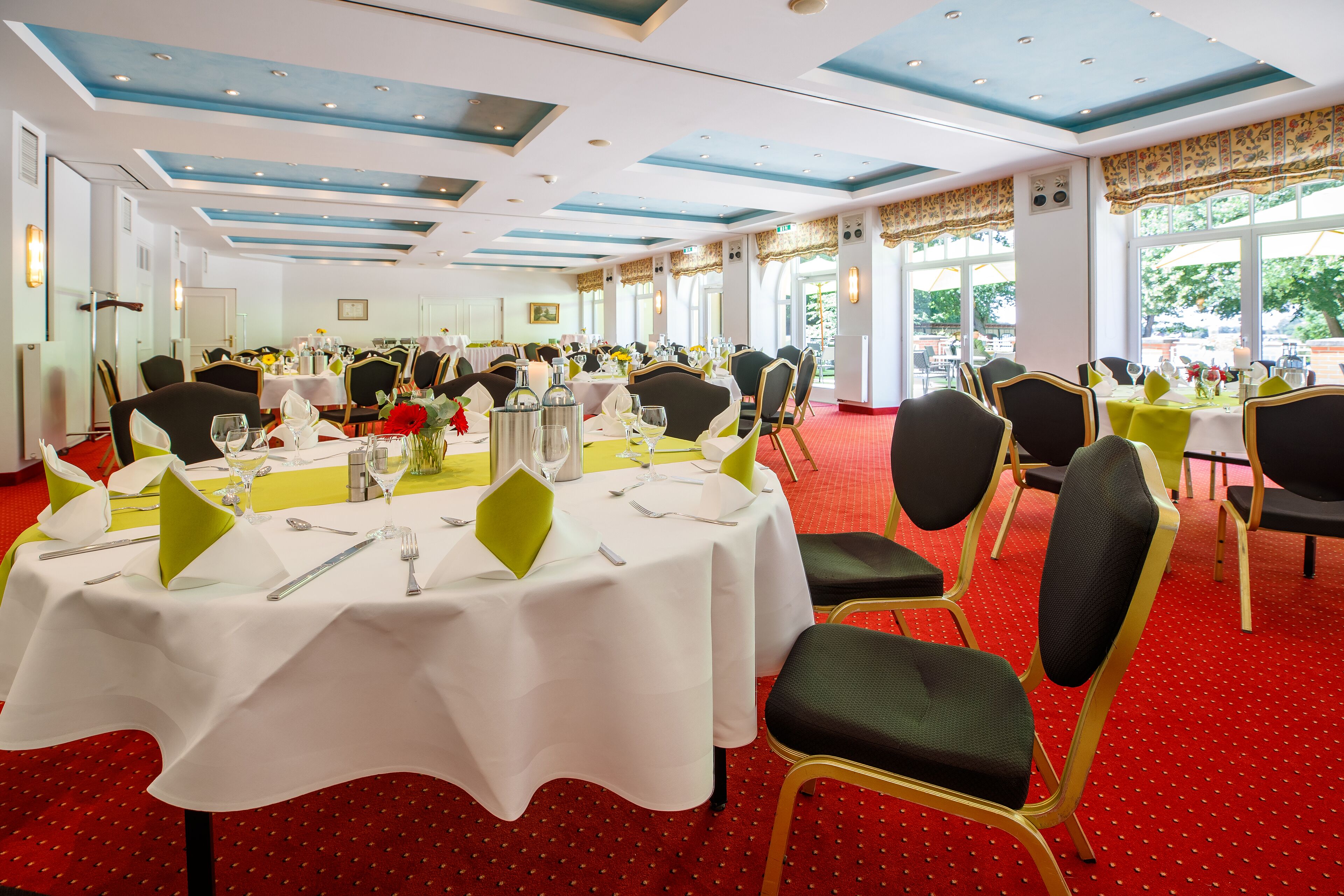 Un salón de banquetes con mesas redondas, sillas y un suelo cubierto de alfombra roja.
